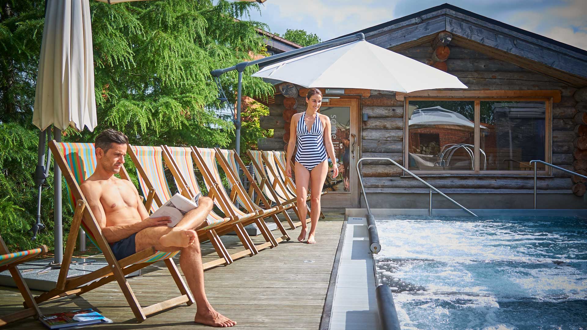 man reading woman walking poolside wooden cabin summer